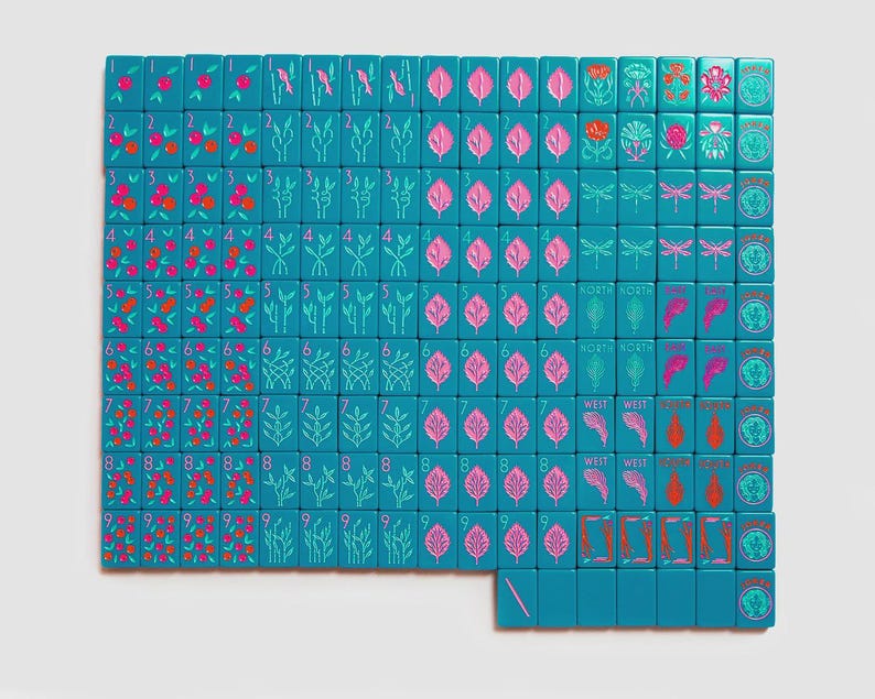 K&ouml;nnte beinhalten: Ein Set aus blaugr&uuml;nen Mahjong-Spielsteinen in einem Raster angeordnet, mit eingravierten Motiven von nummerierten Fr&uuml;chten, botanischen Elementen, Libellen, Himmelsrichtungen und Joker-Steinen, verziert mit rosa, roter und hellblauer Tinte.