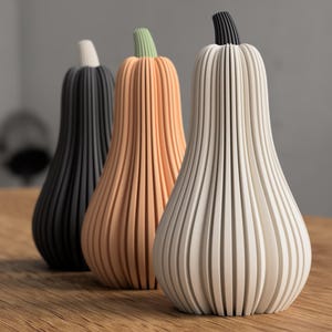 Peut inclure: Trois vases décoratifs en forme de courge alignés. Les vases sont faits de lattes verticales, avec un code couleur noir, orange et blanc. Les tiges sont noires, vertes et blanches. Les vases sont sur une surface en bois.