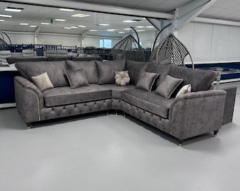 May include: A large, grey corner sofa with multiple cushions and a button-tufted base. The sofa has a curved design and is accented with decorative pillows. The room has a neutral colour palette and is well-lit.