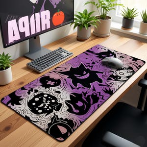 May include: A rectangular purple and black mousepad featuring cartoon ghost characters. The mousepad is on a wooden desk with a computer monitor, keyboard, and mouse. The monitor displays the word "AUR" in white.