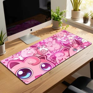 Könnte beinhalten: Eine rechteckige, rosa Schreibtischunterlage mit einem sich wiederholenden Muster von Cartoon-Charakteren in verschiedenen Rosatönen. Die Charaktere haben große Augen und sind vor einem hellrosa Hintergrund platziert. Die Matte liegt auf einem Holztisch.