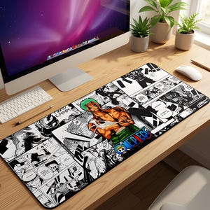 May include: Black and white manga-style desk mat featuring a colorful illustration of a character with green hair and the text "ONE PIECE". The mat is rectangular and designed to fit under a keyboard and mouse.