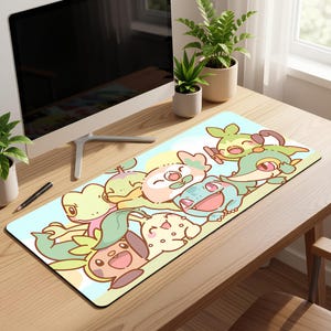 May include: A rectangular desk mat featuring a cartoon illustration of several colorful, smiling creatures. The mat has a light blue background with a yellow sun and a black border. The creatures are in shades of green, pink, and yellow.