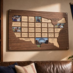 Könnte beinhalten: Ein rechteckiges Wanddisplay aus Holz in Form der Landkarte der Vereinigten Staaten mit einem Raster aus Fächern für Fotos und Textbeschriftungen von MLB-Stadien. Das dunkle Holzbrett trägt den eingravierten Text MLB STADIUM TOUR und silberne Beschläge.