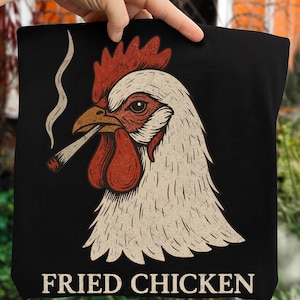 May include: Black tote bag with a graphic of a rooster smoking a cigarette. The rooster has a red comb and wattle, with a white and tan feathered head. The words "FRIED CHICKEN" are printed in white at the bottom of the bag.