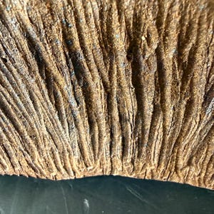 Pu&ograve; includere: Una vista ravvicinata di una superficie in ceramica marrone testurizzata con profondi solchi e creste verticali. Il materiale ha un aspetto ruvido e terroso con variazioni di tono che vanno dal beige chiaro al marrone scuro.
