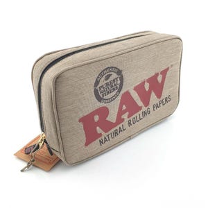 Pu&ograve; includere: Un astuccio rettangolare beige con cerniera e la scritta "RAW NATURAL ROLLING PAPERS" in rosso. L'astuccio presenta anche un logo circolare con le parole "AUTHENTIC PUREST NATURAL FIBERS UNREFINED". Un piccolo cartellino &egrave; attaccato alla cerniera.
