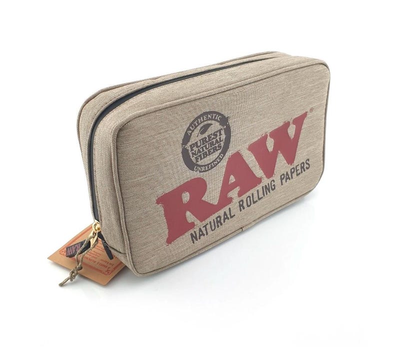 Pu&ograve; includere: Un astuccio rettangolare beige con cerniera e la scritta "RAW NATURAL ROLLING PAPERS" in rosso. L'astuccio presenta anche un logo circolare con le parole "AUTHENTIC PUREST NATURAL FIBERS UNREFINED". Un piccolo cartellino &egrave; attaccato alla cerniera.