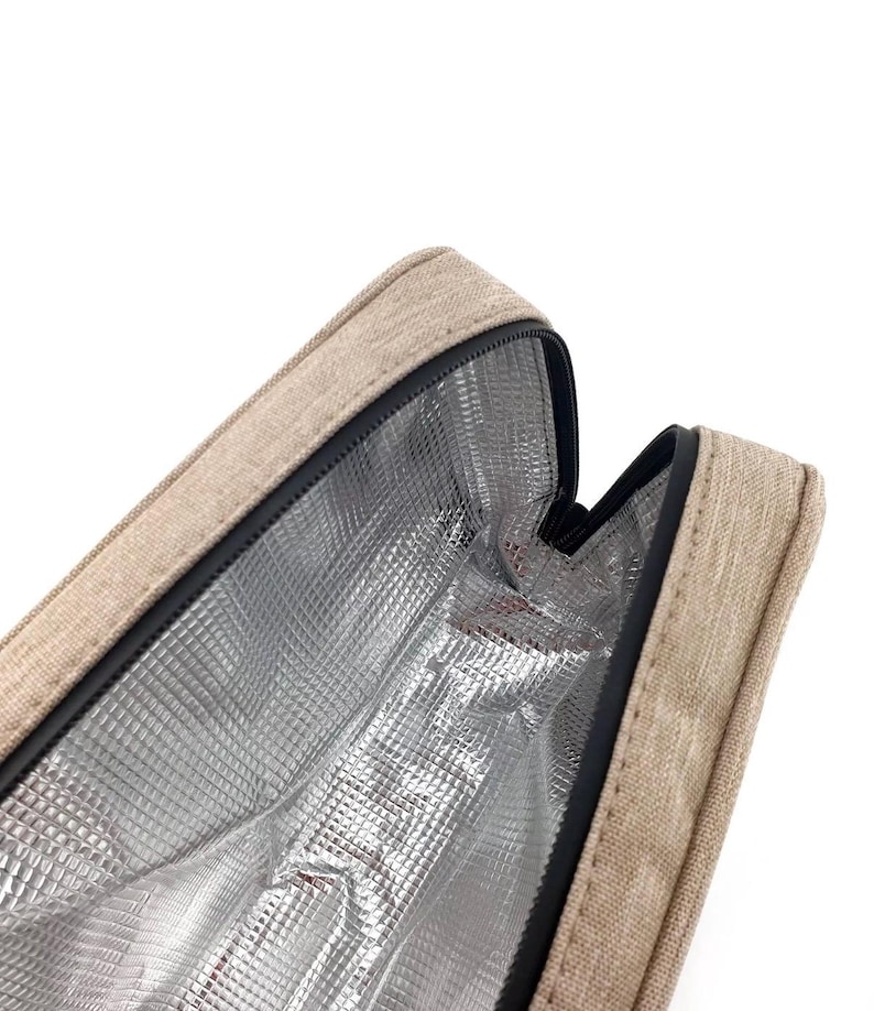 Pu&ograve; includere: Borsa termica beige con cerniera nera e interno in lamina argentata. La borsa &egrave; aperta, rivelando la fodera interna. L'esterno ha un aspetto strutturato.