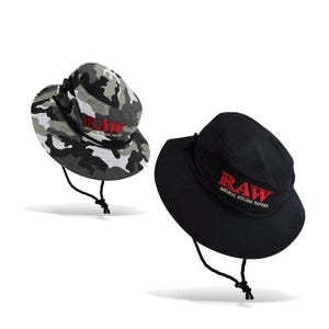 May include: Two bucket hats. One is black with red embroidered text that reads "RAW NATURAL ROLLING PAPERS." The other hat has a camouflage pattern with the same red text. Both hats have a black chin strap.