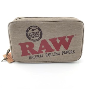 May include: A rectangular, beige travel bag with the word "RAW" in large, maroon letters. The bag features the text "AUTHENTIC PUREST NATURAL FIBERS UNREFINED" and "NATURAL ROLLING PAPERS". A small tag is attached to the zipper.