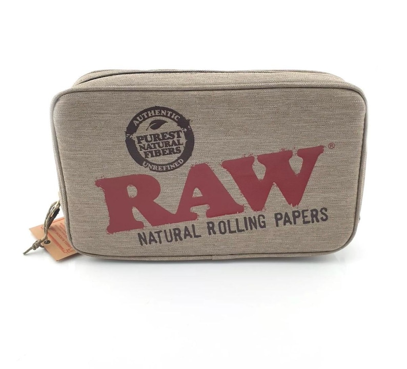 Pu&ograve; includere: Una borsa da viaggio rettangolare, color beige, con la scritta "RAW" a grandi lettere color marrone. La borsa presenta il testo "AUTHENTIC PUREST NATURAL FIBERS UNREFINED" e "NATURAL ROLLING PAPERS". Una piccola etichetta &egrave; attaccata alla cerniera.