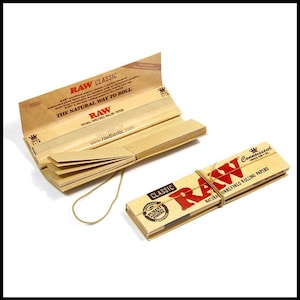 May include: Two packs of RAW Classic rolling papers. One pack is open, displaying the papers and the text "RAW CLASSIC THE NATURAL WAY TO ROLL." The other pack is closed and secured with a rubber band, with the text "RAW" in red.