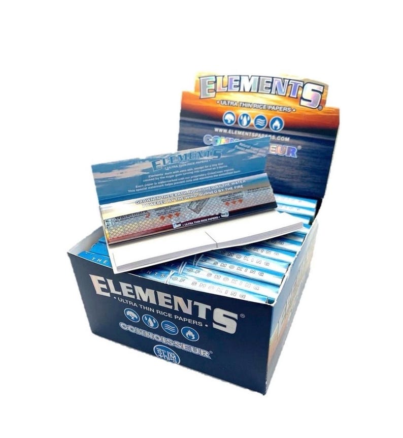 May include: A box of Elements ultra-thin rice papers. The box is dark blue with white text and graphics. The box is open, revealing stacks of the rice papers. The box also has a lid with the Elements logo and text.