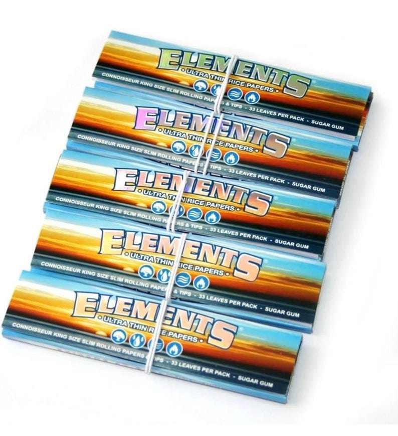 May include: A stack of Elements ultra-thin rice rolling paper packs. Each pack features a sunset design with the brand name in a bold, colorful font. The text includes "Connoisseur King Size Slim Rolling Papers & Tips - 33 Leaves Per Pack - Sugar Gum."
