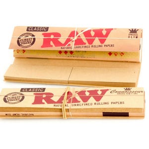 Puede incluir: Dos paquetes de papel de liar RAW Classic. El embalaje es de color beige con texto rojo que dice "RAW" y "NATURAL UNREFINED ROLLING PAPERS". La pila superior est&aacute; atada con hilo natural. El texto "CLASSIC" est&aacute; impreso en la parte superior.