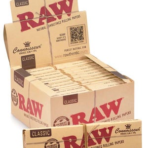 Puede incluir: Una caja expositora y una caja m&aacute;s peque&ntilde;a de papel de liar RAW Classic King Size Slim + Tips. Las cajas son de color beige con texto y logotipos rojos. El texto incluye "RAW", "Classic" y "Natural Unrefined Rolling Papers". Las cajas est&aacute;n atadas con hilo.