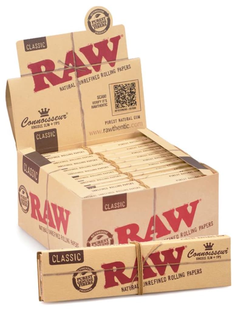 Puede incluir: Una caja expositora y una caja m&aacute;s peque&ntilde;a de papel de liar RAW Classic King Size Slim + Tips. Las cajas son de color beige con texto y logotipos rojos. El texto incluye "RAW", "Classic" y "Natural Unrefined Rolling Papers". Las cajas est&aacute;n atadas con hilo.