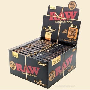 Puede incluir: Una caja negra de papel de liar RAW Classic, con el texto "RAW" en rojo. La caja también muestra "Black" y "Connoisseur" y un código QR. La caja está llena de paquetes individuales de papel de liar.