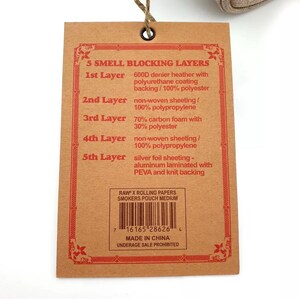 Pu&ograve; includere: Un'etichetta di carta marrone con bordi decorativi rossi e testo che descrive cinque strati di materiali che bloccano gli odori. L'etichetta include un codice a barre, il testo "RAW x Rolling Papers Smokers Pouch Medium" e "Made in China."