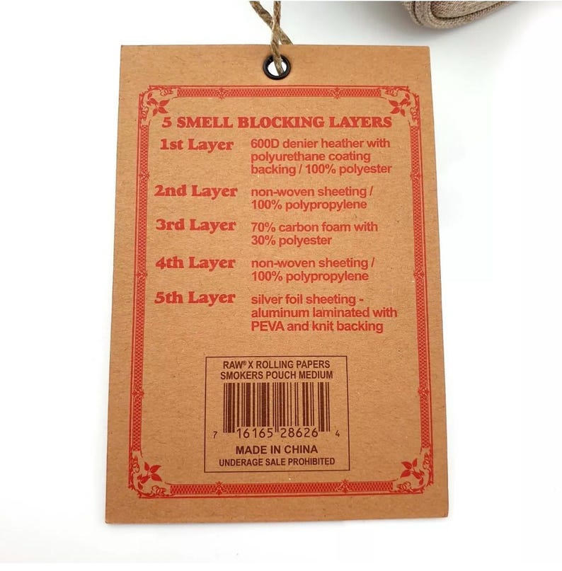Pu&ograve; includere: Un'etichetta di carta marrone con bordi decorativi rossi e testo che descrive cinque strati di materiali che bloccano gli odori. L'etichetta include un codice a barre, il testo "RAW x Rolling Papers Smokers Pouch Medium" e "Made in China."