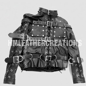 May include: Black leather jacket with multiple straps, buckles, and eyelet details. The jacket features a high collar and is designed with a series of straps across the chest, arms, and waist. The text "HM LEATHER CREATIONS" is visible.