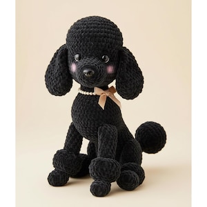 Könnte beinhalten: Ein schwarzer Häkelpudel mit einer Perlenkette und einer beigen Schleife. Der Hund hat rosa Wangen und sitzt aufrecht. Das Fell des Pudels ist strukturiert und der Hund hat einen runden Schwanz.