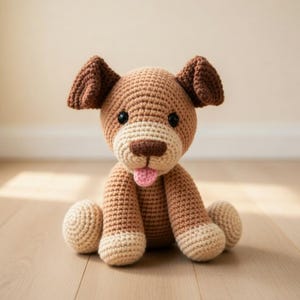 Könnte beinhalten: Ein handgefertigtes Häkelhundespielzeug in Braun- und Cremetönen mit einer rosa Zunge. Der Hund hat dunkle Augen und sitzt auf einem Holzboden. Die Ohren und die Nase sind in einem dunkleren Braunton gehalten.