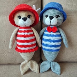 Könnte beinhalten: Zwei handgefertigte Häkelsiegelpuppen. Eine Puppe trägt einen roten Hut und ein rot-weiß gestreiftes Oberteil. Die andere Puppe trägt einen blauen Hut und ein blau-weiß gestreiftes Oberteil mit roter Fliege. Beide haben beige Flossen.