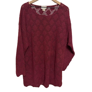 May include: A long-sleeve, deep magenta sweater featuring an open-knit diamond pattern throughout the body and sleeves. The garment has a round neckline and a label at the inner collar that reads Adrian Jordan.