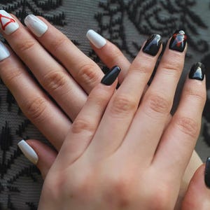 May include: Manicured nails in various designs. Some nails are solid black, while others are white with a gradient effect or a red triangle design. The nails are neatly shaped and polished, showcasing a modern nail art style.