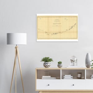 May include: A framed vintage map of the Aleutian Islands, featuring detailed geographical information. The map is printed on aged paper with a beige hue, and is framed in a white border. The map includes text and lines.