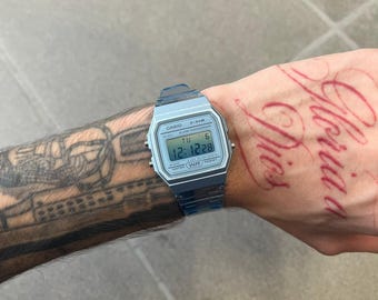May include: A translucent blue digital wristwatch featuring a rectangular face with the text CASIO F-91W ALARM CHRONOGRAPH WATER RESIST. The digital display shows the time 12:12:28, the day TU, and the date 6, with a matching blue resin strap.