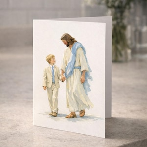 Peut inclure: Carte de vœux pliée avec une illustration à l'aquarelle de Jésus tenant la main d'un jeune garçon. Jésus porte une robe blanche et une écharpe bleue, le garçon un costume beige et une cravate bleue. La carte est sur une surface grise.