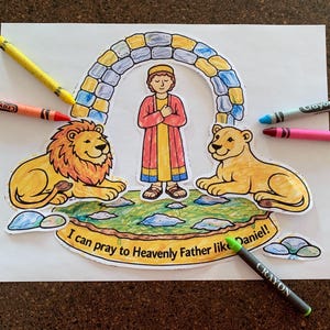 May include: A coloring page featuring a biblical scene with a man, two lions, and an archway. The text "I can pray to Heavenly Father like Daniel!" is included. Crayola crayons in various colors surround the image.