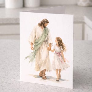 May include: Watercolor illustration on a greeting card. Depicts a figure in a white robe and a green sash holding hands with a girl in a white dress with a pink bow. The figures are walking together.