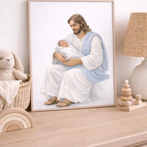 May include: Framed print showing a man with long brown hair and a beard, in white robes and a blue sash, holding a baby wrapped in white. The artwork is in a wooden frame, on a light-coloured wooden surface. A wicker basket and a lamp are visible.