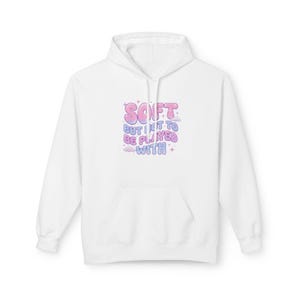 Può includere: Felpa con cappuccio bianca con tasca frontale e cappuccio con coulisse. La parte anteriore della felpa con cappuccio presenta la scritta "SOFT but I get to be played with" in lettere rosa, blu e viola con stelle e nuvole.