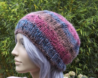May include: A striped knit beanie hat in shades of pink, brown, and blue. The hat is made of a soft, textured yarn and has a slouchy fit.