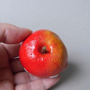 Puede incluir: Una manzana decorativa pintada a mano, con un degradado rojo y amarillo vibrante. La manzana presenta un peque&ntilde;o tallo marr&oacute;n y una superficie texturizada. Este art&iacute;culo artesanal es una pieza &uacute;nica de decoraci&oacute;n del hogar.