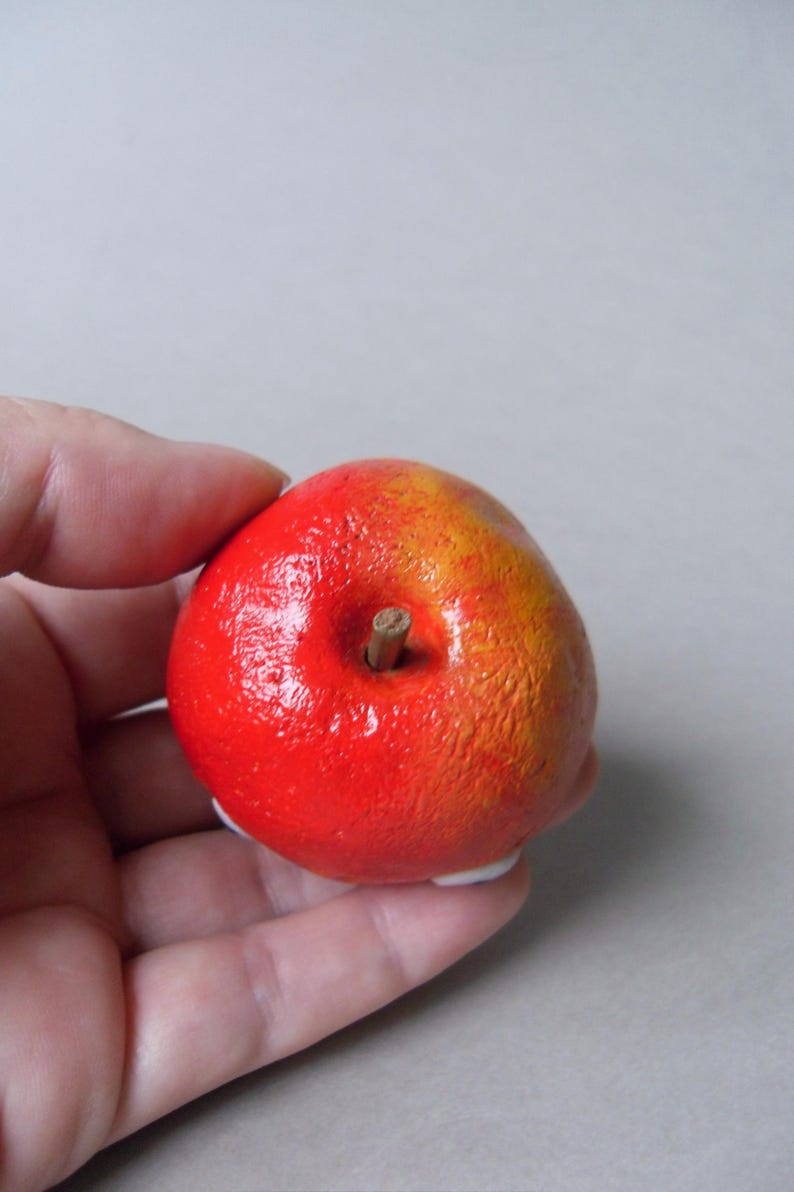 Puede incluir: Una manzana decorativa pintada a mano, con un degradado rojo y amarillo vibrante. La manzana presenta un peque&ntilde;o tallo marr&oacute;n y una superficie texturizada. Este art&iacute;culo artesanal es una pieza &uacute;nica de decoraci&oacute;n del hogar.