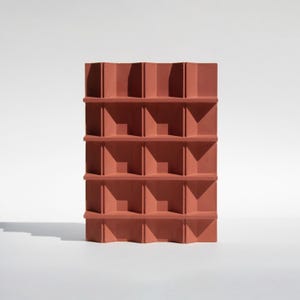 May include: A terracotta-coloured, geometric shelf unit with a repeating pattern of angled shelves and vertical supports. The design creates a series of open cubbies. The unit casts a shadow on a white surface.
