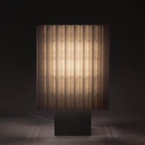 May include: A rectangular table lamp featuring a pleated, semi-translucent white shade that emits a soft, warm glow. The lamp is supported by a solid, dark-colored square base, creating a clean, vertical silhouette with distinct light and shadow.