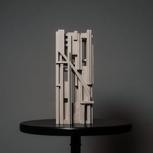 May include: A light gray, rectangular sculpture composed of multiple vertical and horizontal bars of varying lengths and thicknesses. The structure features a prominent diagonal bar crossing the center, creating a complex, layered, and open geometric form.