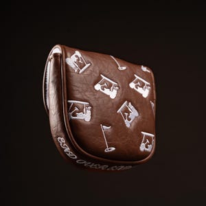 May include: A brown golf putter head cover with white embroidered golf-themed designs. The cover features a repeating pattern of golf carts, flags, and golfers. The words "End Over End" are embroidered in white along the bottom edge.