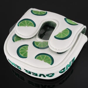 Pu&ograve; includere: Un copritesta per putter da golf bianco con un motivo ripetuto di fette di lime verdi. La copertura presenta una patta di chiusura magnetica e la scritta END OVER END ricamata in verde lungo il bordo laterale del materiale sintetico.