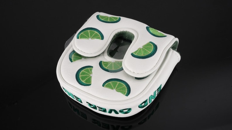 Pu&ograve; includere: Un copritesta per putter da golf bianco con un motivo ripetuto di fette di lime verdi. La copertura presenta una patta di chiusura magnetica e la scritta END OVER END ricamata in verde lungo il bordo laterale del materiale sintetico.
