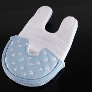 May include: A baby bib with a light blue front featuring white embroidered stars. The bib has a white, absorbent interior and a curved shape to fit around the neck. The bib is designed to catch spills and dribbles.