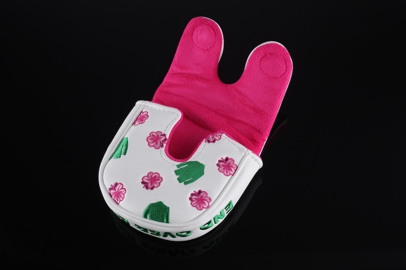 Puede incluir: Una funda para putter tipo mallet de color blanco con un patr&oacute;n de flores rosas y cactus verdes. El interior est&aacute; forrado con tela de color rosa brillante. El lateral de la funda muestra el texto bordado en verde END OVER END.