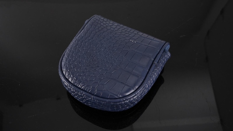 May include: A small, navy blue coin purse with a rounded, U-shaped silhouette. The exterior features a textured, embossed crocodile skin pattern across the entire surface, including the curved edges and the top flap closure.